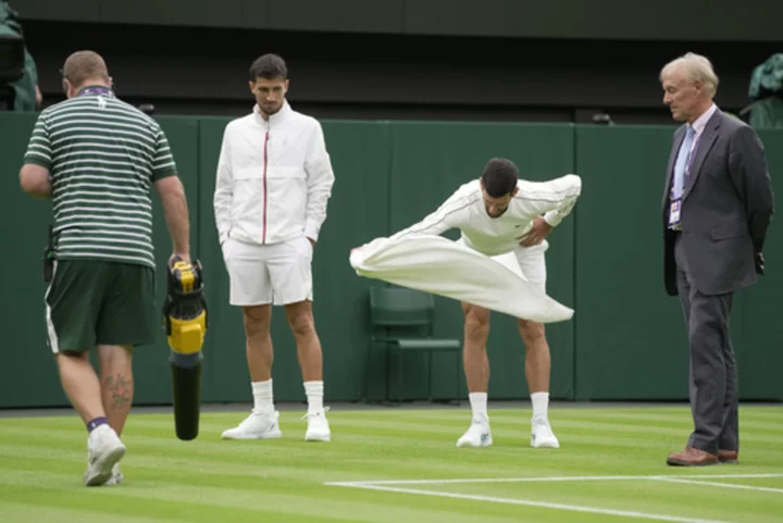 Novak Djokovic uses his towel at Wimbledon to help dry the Centre Court grass after a rain delay