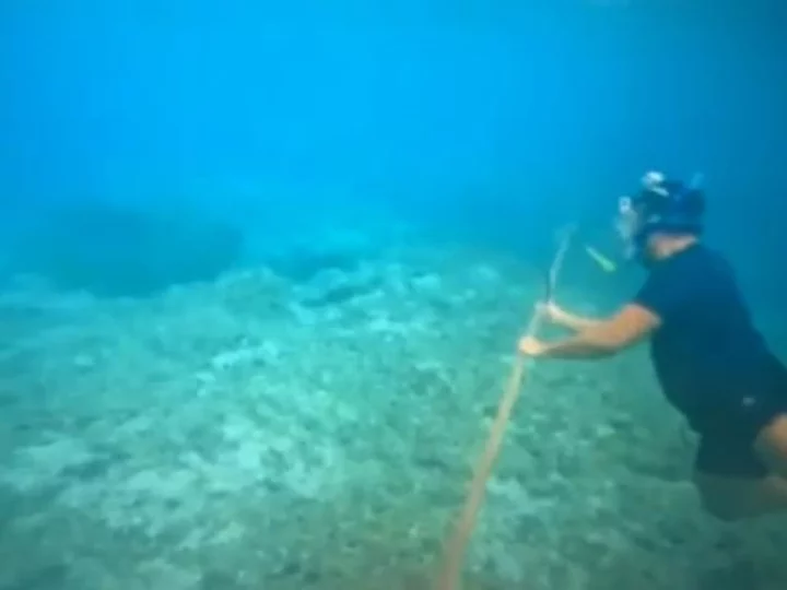 Filipino diver with a knife helps remove floating barrier installed by China in South China Sea